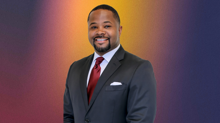 A professional portrait of a man in a dark suit and red tie, smiling against a multicolored background.