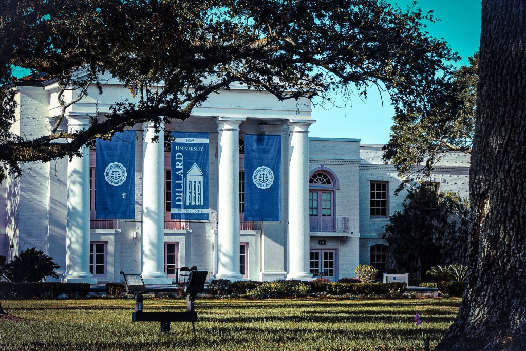 Exterior view of Dillard University showcasing its iconic columns and blue banners against a clear sky, with green grass and trees in the foreground.