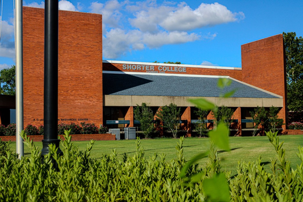 Exterior view of Shorter College featuring a brick building with a sloped roof, landscaped grass, and greenery in the foreground.