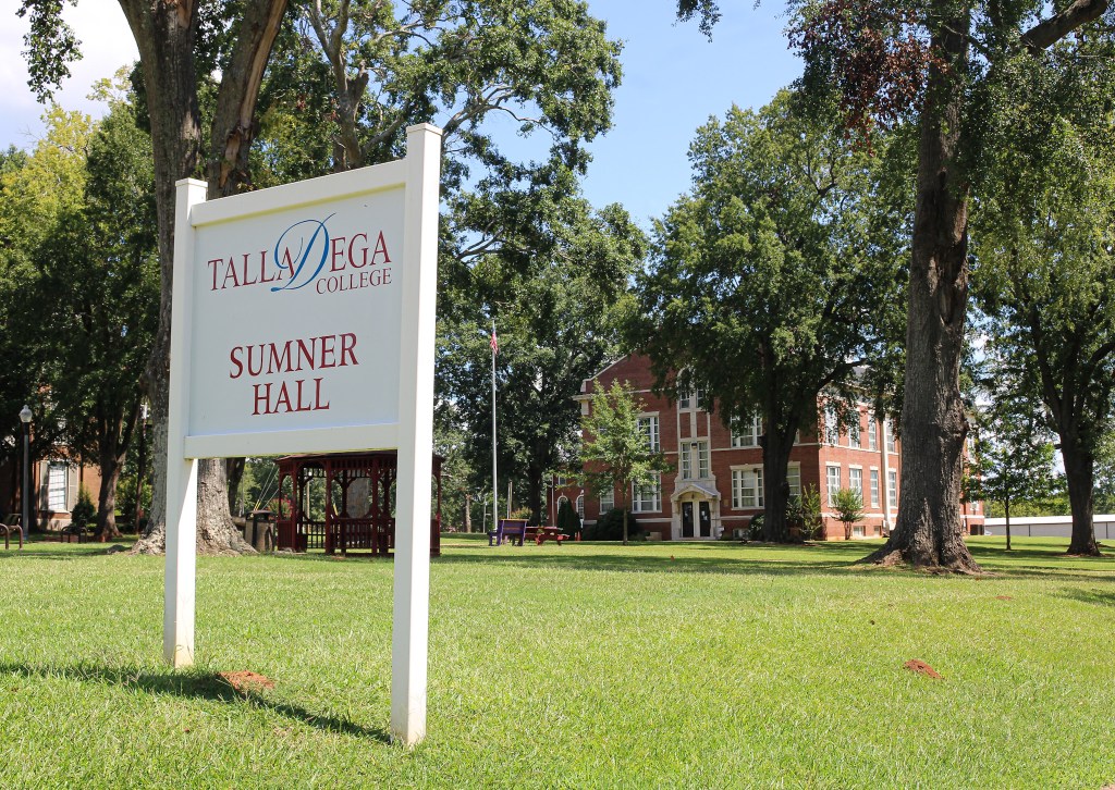 A sign for Sumner Hall at Talladega College, surrounded by green grass and trees, with the building visible in the background.